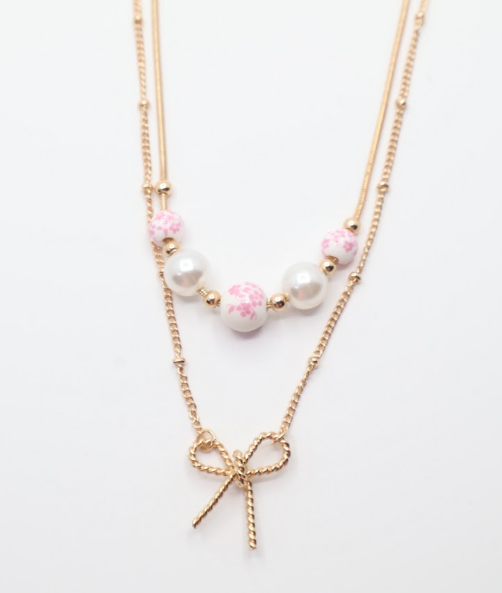 Bow & Bead Layered Necklace. This layered design features a dainty gold-tone bow pendant on one chain and pocelain white beads with pink floral print.