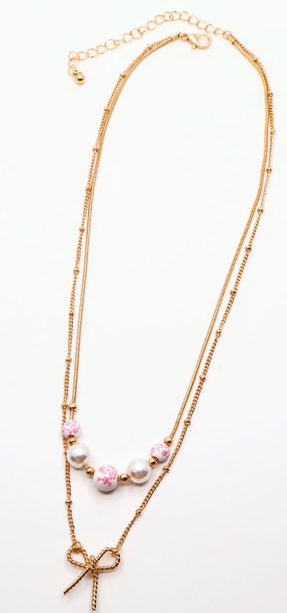 Bow & Bead Layered Necklace. This layered design features a dainty gold-tone bow pendant on one chain and pocelain white beads with pink floral print.