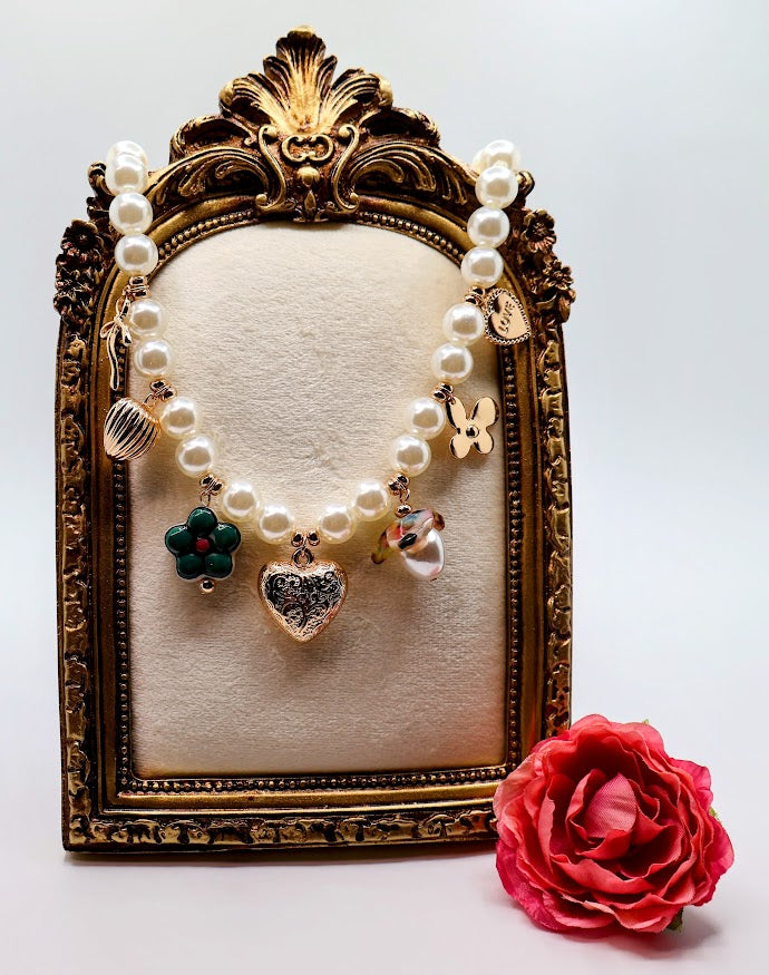 Pearl Charm Necklace is a graceful blend of timeless elegance and whimsical charm. Featuring a strand of lustrous pearls adorned with delicate gold-tone charms, including hearts, flowers, and a touch of sparkle.
