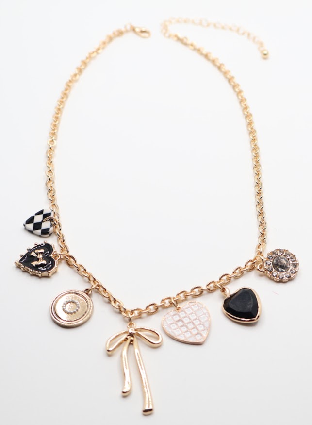 Charm Necklace is a whimsical and eye-catching accessory, perfect for adding character to any outfit. This necklace features a series of unique charms, including hearts, a bow, a sparkling gem, and intricate patterns, all beautifully arranged on a gold-tone chain.