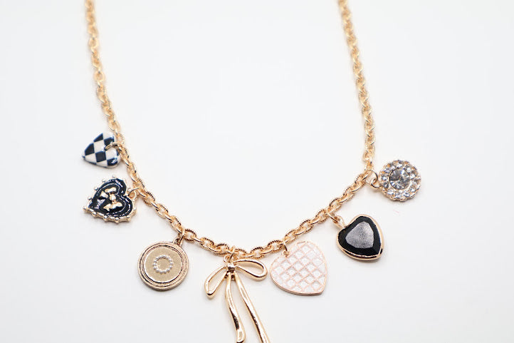 Charm Necklace is a whimsical and eye-catching accessory, perfect for adding character to any outfit. This necklace features a series of unique charms, including hearts, a bow, a sparkling gem, and intricate patterns, all beautifully arranged on a gold-tone chain.