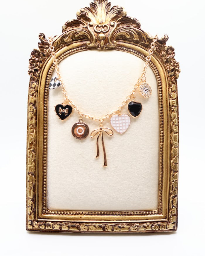 Charm Necklace is a whimsical and eye-catching accessory, perfect for adding character to any outfit. This necklace features a series of unique charms, including hearts, a bow, a sparkling gem, and intricate patterns, all beautifully arranged on a gold-tone chain.