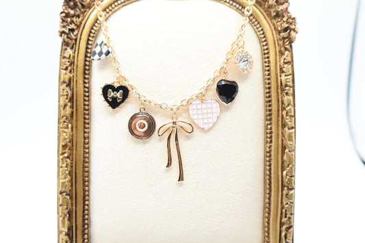 Charm Necklace is a whimsical and eye-catching accessory, perfect for adding character to any outfit. This necklace features a series of unique charms, including hearts, a bow, a sparkling gem, and intricate patterns, all beautifully arranged on a gold-tone chain.