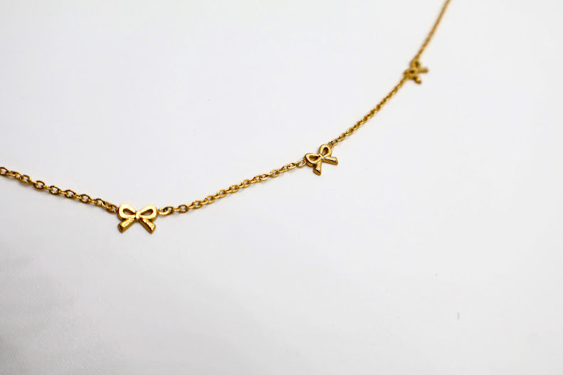 Gold Bow Charm Necklace is a delicate and timeless accessory that exudes elegance and charm. Featuring three dainty bow-shaped accents.