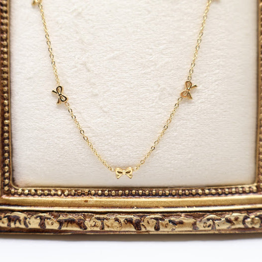 Gold Bow Charm Necklace is a delicate and timeless accessory that exudes elegance and charm. Featuring three dainty bow-shaped accents.