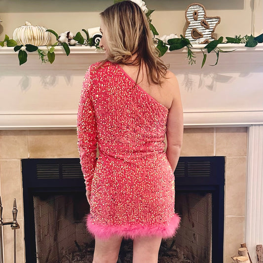 Person wearing a pink sequin dress with feather details in front of a decorated fireplace.