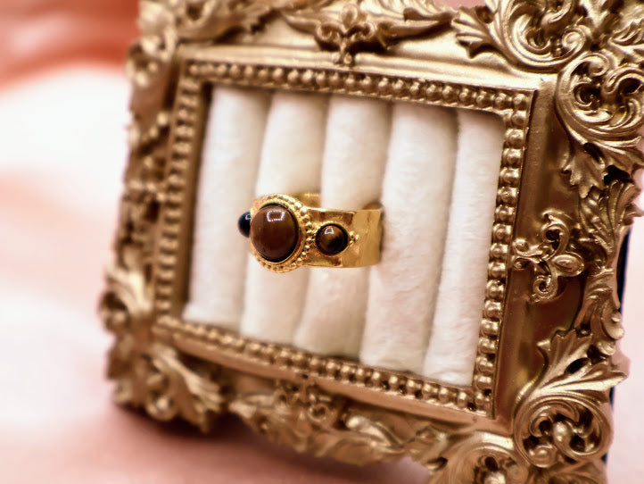 Ring is a captivating blend of warmth and mystique, making it a standout addition to any jewelry collection. Featuring a luminous round amber-toned centerpiece flanked by two smaller dark accent stones.