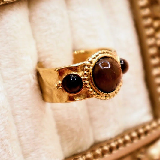 Ring is a captivating blend of warmth and mystique, making it a standout addition to any jewelry collection. Featuring a luminous round amber-toned centerpiece flanked by two smaller dark accent stones.