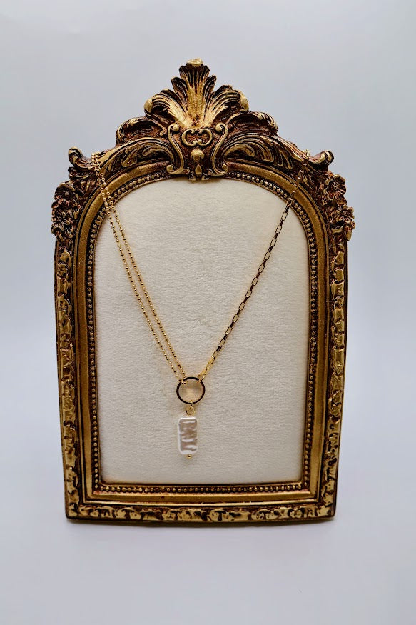 Pendant Necklace is a chic and modern accessory that embodies effortless style. Featuring a stunning rectangular pearl-like charm suspended from a sleek gold-tone ring.