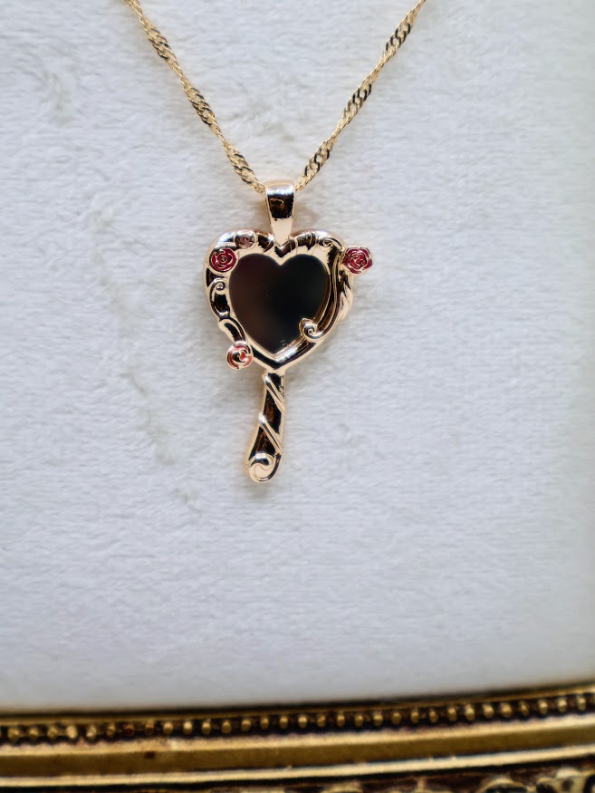ose Mirror Necklace is a stunning symbol of elegance and charm. The heart-shaped pendant, designed as a petite mirror, features intricate gold swirls and delicate pink rose accents that add a romantic touch.