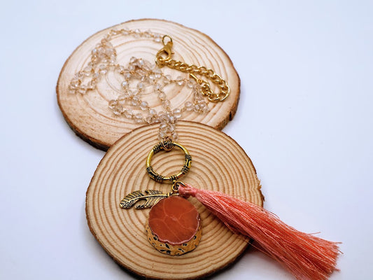Gold toned necklace featuring a rosy coral stone, a dreamy tassel, and a delicate feather charm.