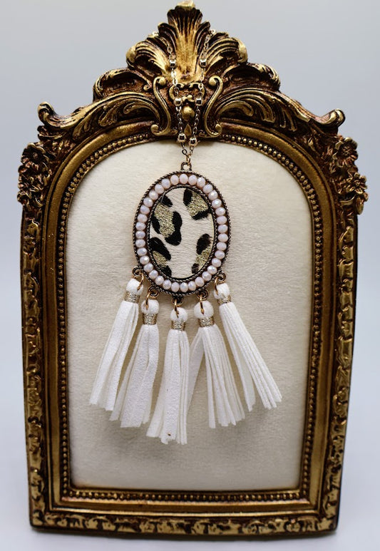 Necklace featuring a bold leopard-print pendant framed in gold and accented with playful white tassels.