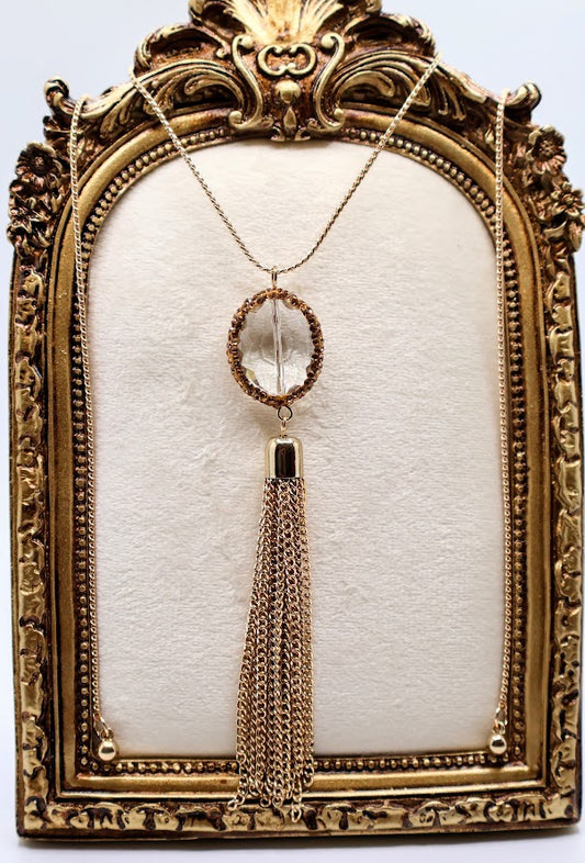 Gold necklace. This radiant piece features a crystal pendant encircled by intricate gold detailing, perfectly complemented by a cascading golden tassel.