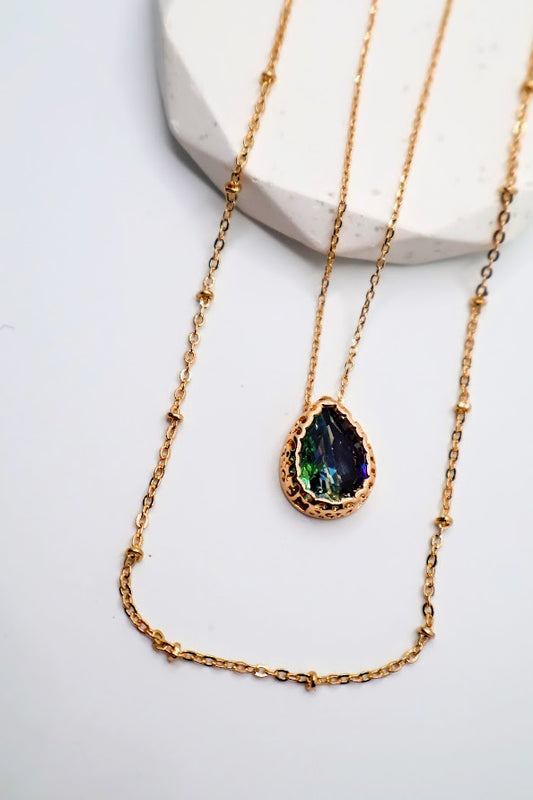 This enchanting layered piece features a stunning teardrop pendant that sparkles with vibrant colors, elegantly suspended between delicate gold chains.