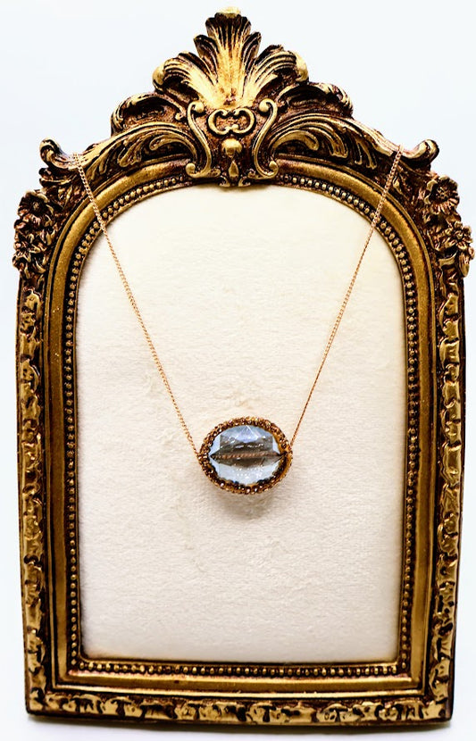 Necklace with a gleaming oval crystal framed in a warm golden setting, suspended from a fine gold chain.