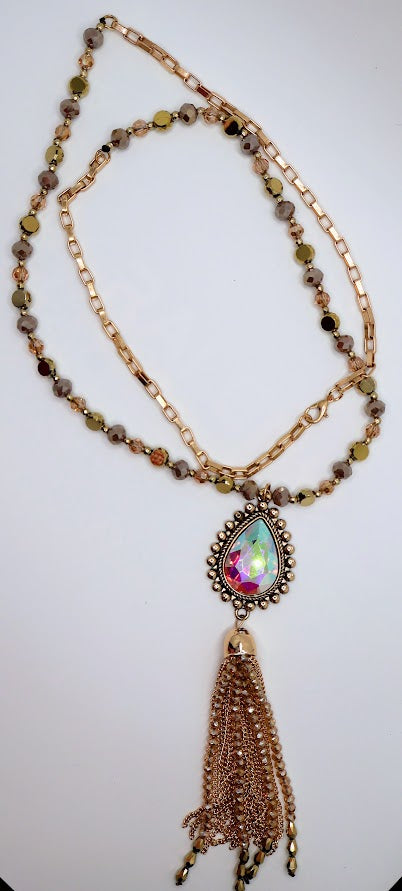 Prismatic Elegance Tassel Necklace features a mesmerizing teardrop crystal pendant with a radiant rainbow shimmer, delicately framed by intricate golden beading.