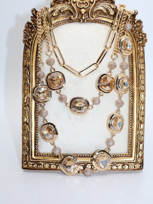 A layered necklace, a combination of intricate gold medallions, pearly accents, and chic layered chains.