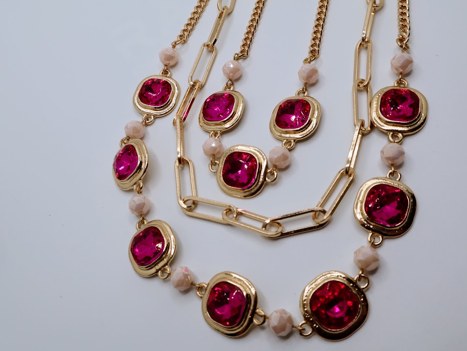 A layered necklace, featuring vibrant ruby-red gems, gold-tone chains, and marbled bead accents.