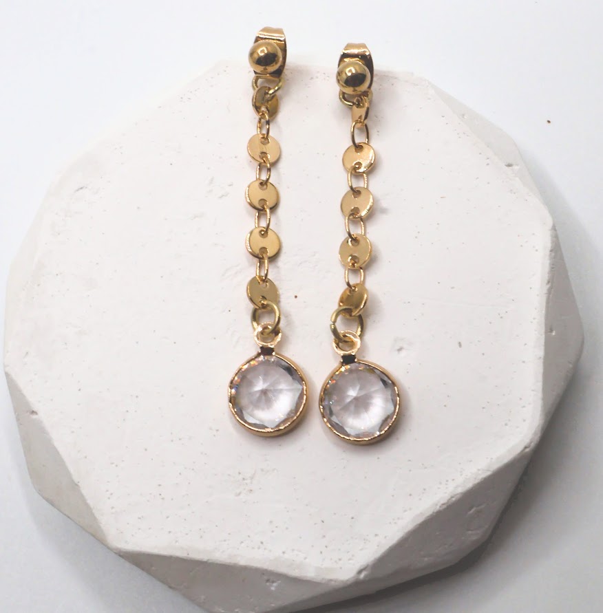 Gold chain earrings with round gemstones on a white stone surface