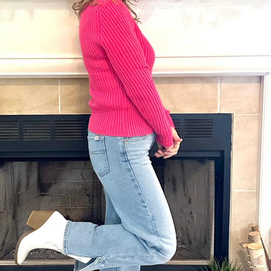 Person wearing a pink sweater and blue jeans standing in front of a fireplace.