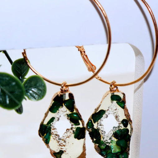 Gold hoop earrings with green and clear teardrop-shaped stone earrings.