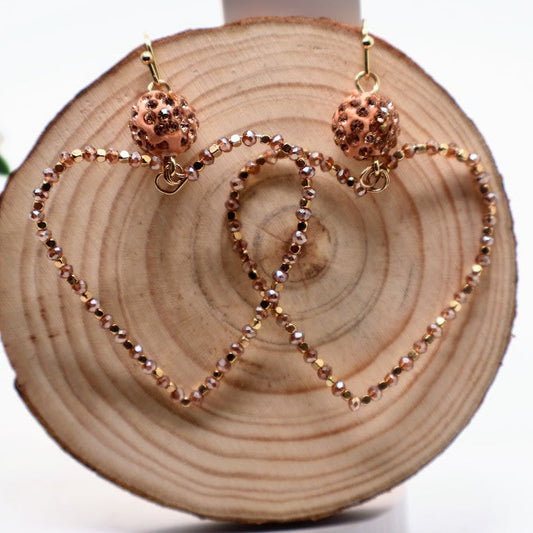 Rose gold heart-shaped earrings on a wooden block