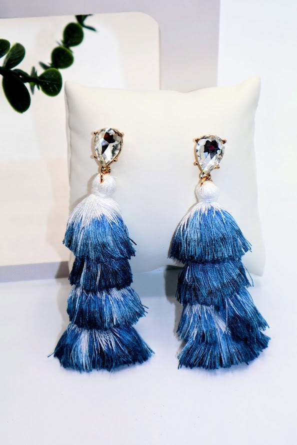 Blue tiered tassel earrings on a white surface with a blurred background