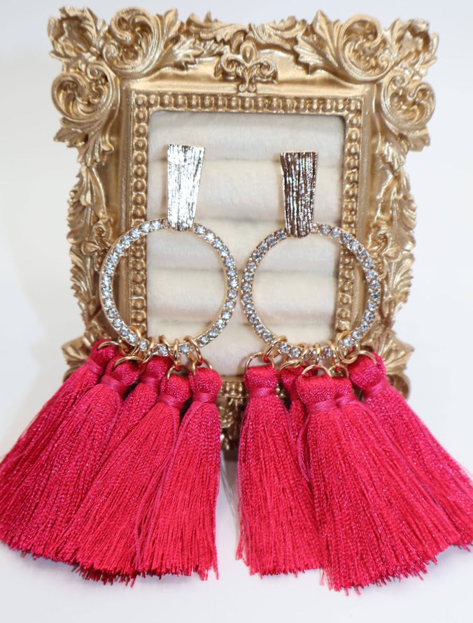 Pink tassel earrings with crystal accents in front of a decorative gold frame.