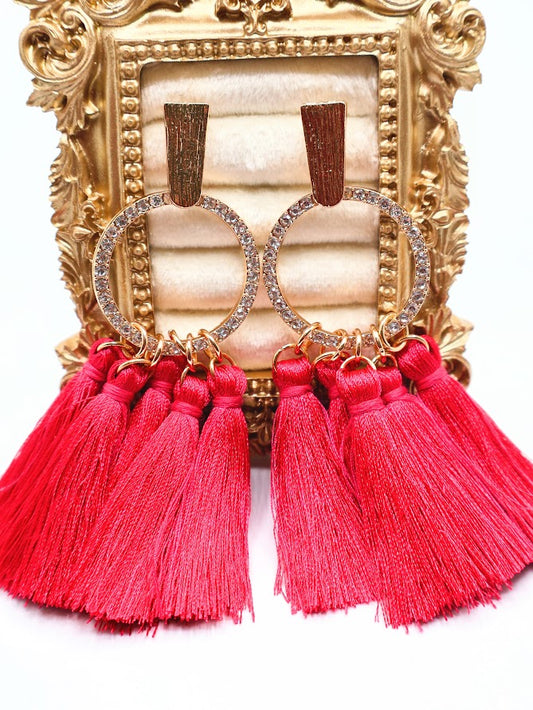 A pair of gold earrings. Featuring bold hot pink tassels suspended from a gold-textured hoop.