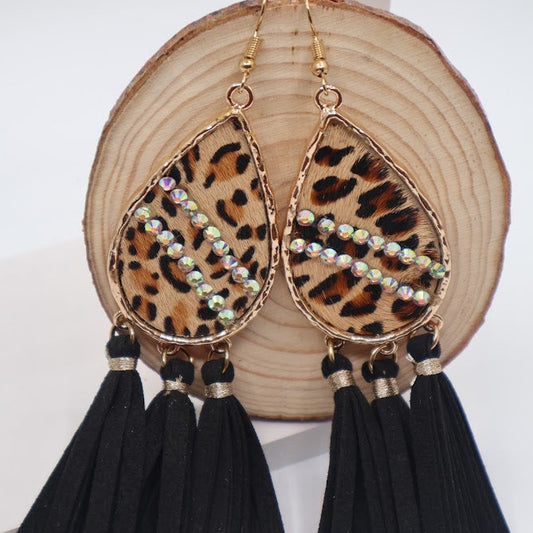 Leopard print teardrop earrings with black tassels on a wooden surface