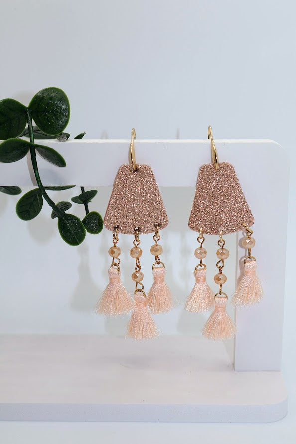 Rose gold tassel earrings on a white stand with a plant in the background