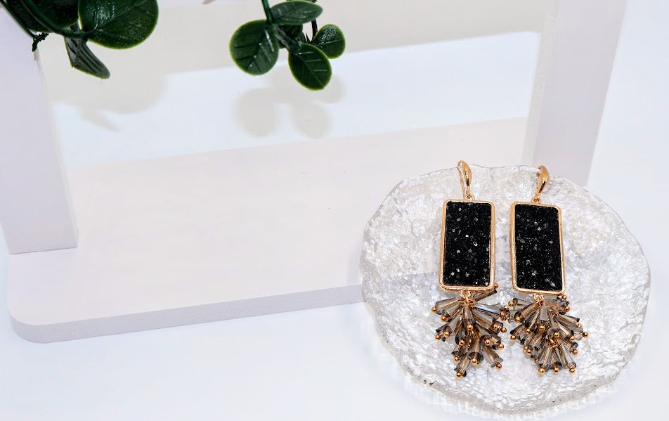 Black and gold earrings on a decorative stand with a white background
