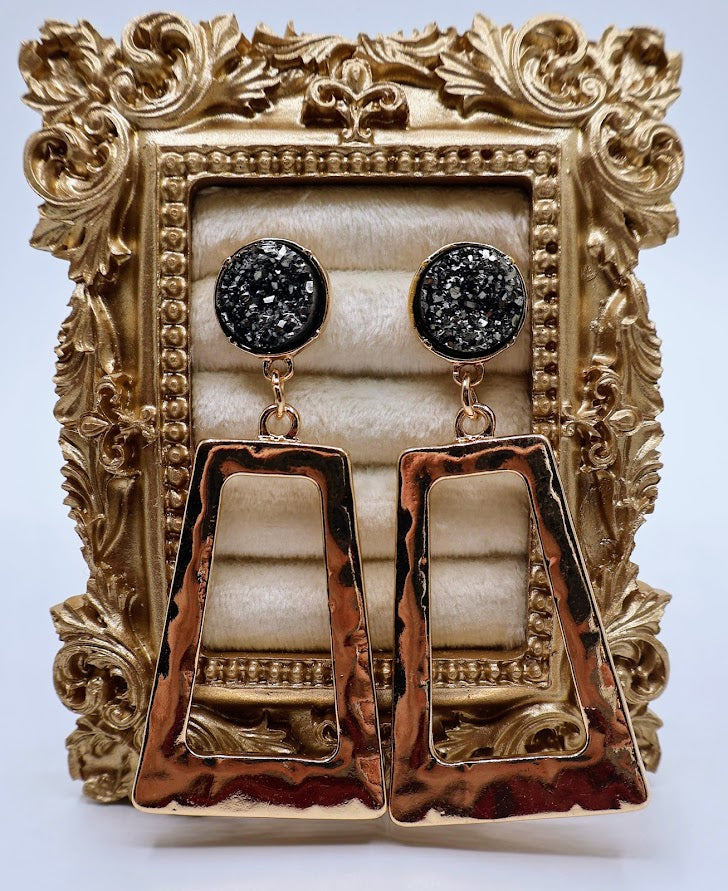 Pair of gold and gray earrings displayed in an ornate gold frame.