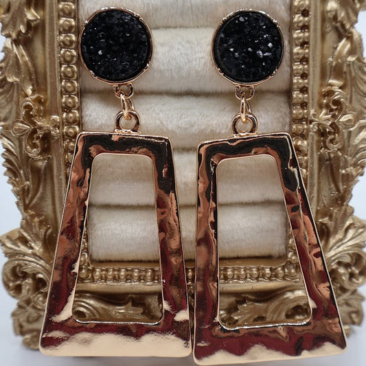 Gold and black earrings on a decorative stand
