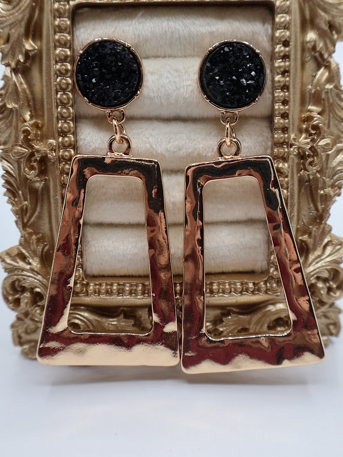 Gold and black earrings on a decorative stand