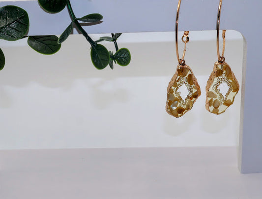 Gold earrings on a white surface with a green leafy branch in the background