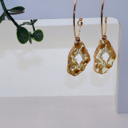 Gold earrings on a white surface with a green leafy branch in the background