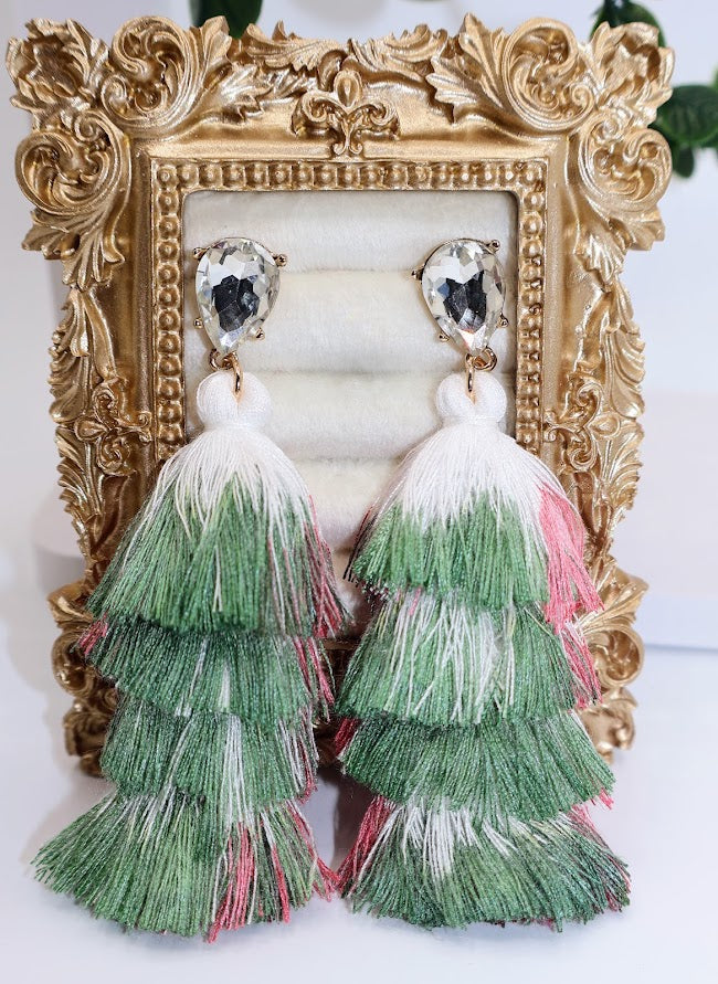 Green and pink tiered tassel earrings in front of an ornate gold frame.