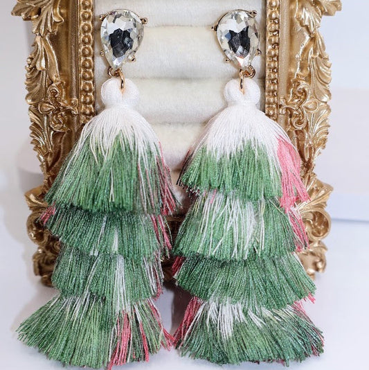 Green and pink tiered tassel earrings in front of an ornate gold frame.