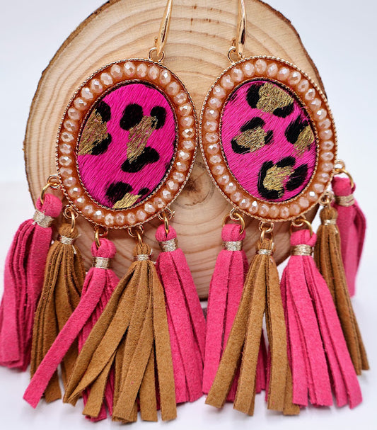 A pair of earrings feature a chic blend of bold pink and earthy brown tassels, elegantly framed by a dazzling gold outline.