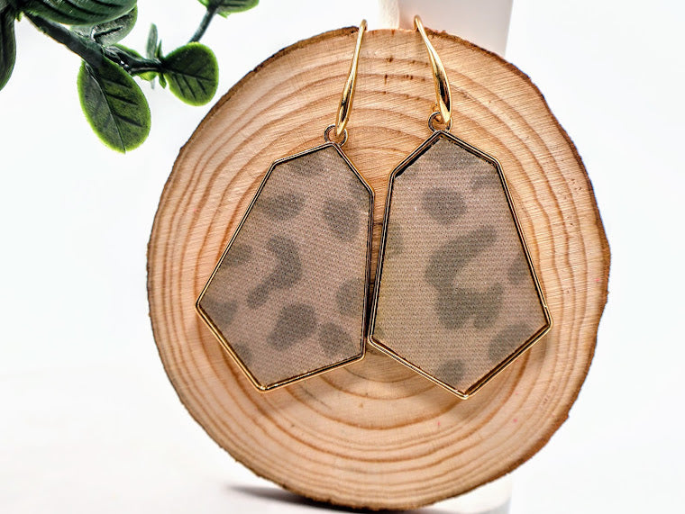 Geometric earrings on a wooden surface with a plant in the background