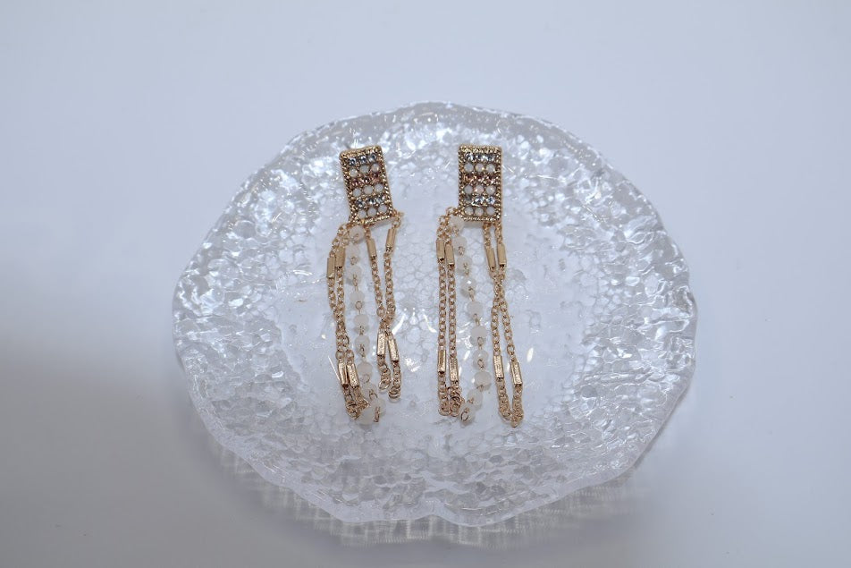 Gold earrings with clear stones on a textured white surface