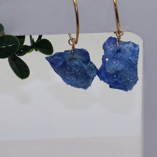 Blue stone earrings on a white card with green leaves in the background