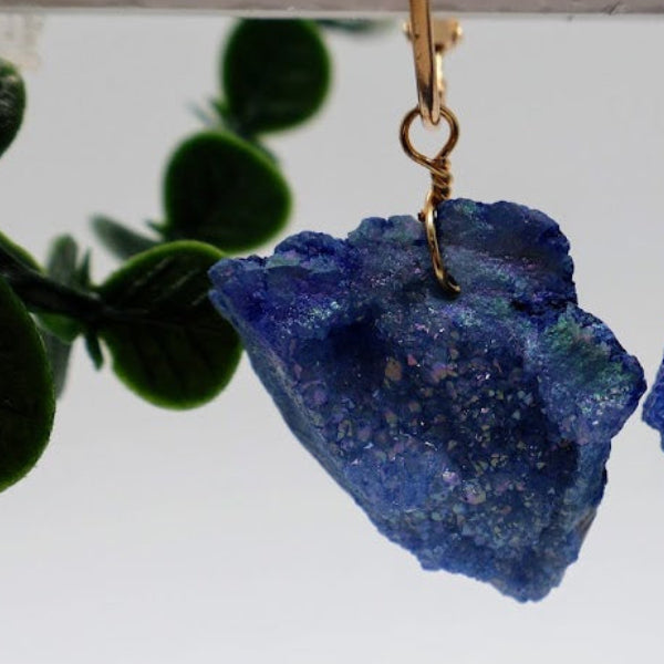 Blue crystal earrings on a white background with green leaves.