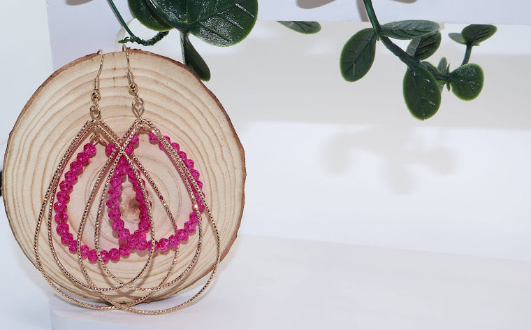 Pair of gold and pink beaded earrings on a wooden disc with a white background