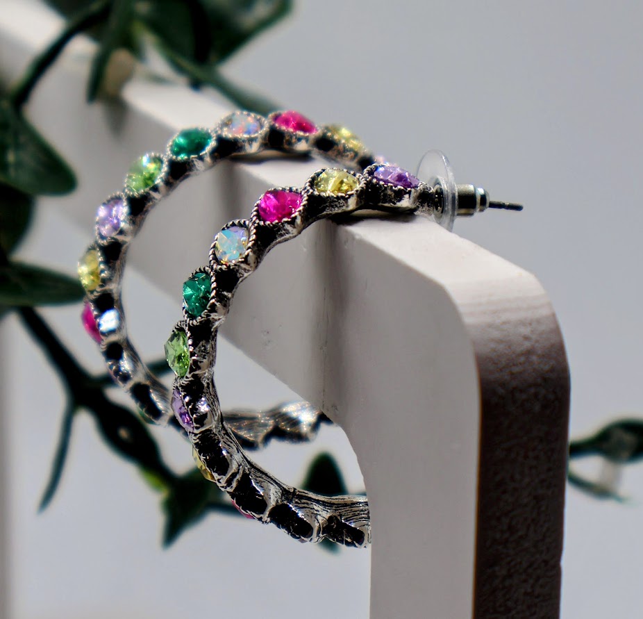 Hoop earrings with colorful gemstones on a white surface with green leaves in the background