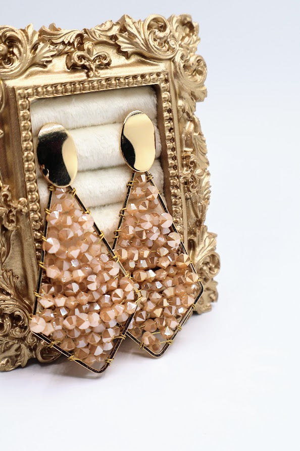 Pair of gold and beige earrings on a decorative gold stand.