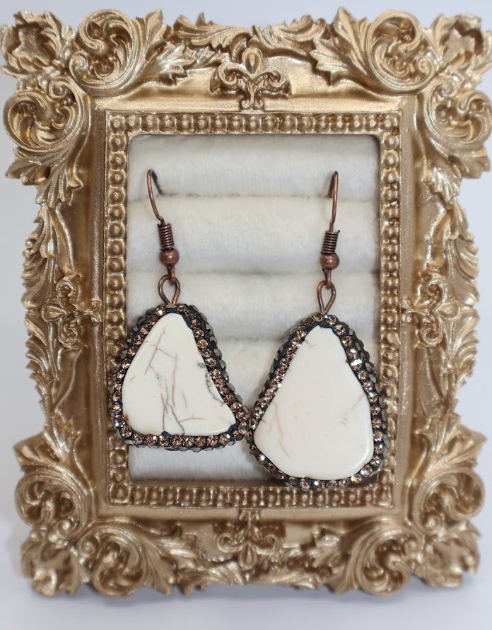 Pair of earrings with cream stone drops surrounded by sparkling metallic accent.