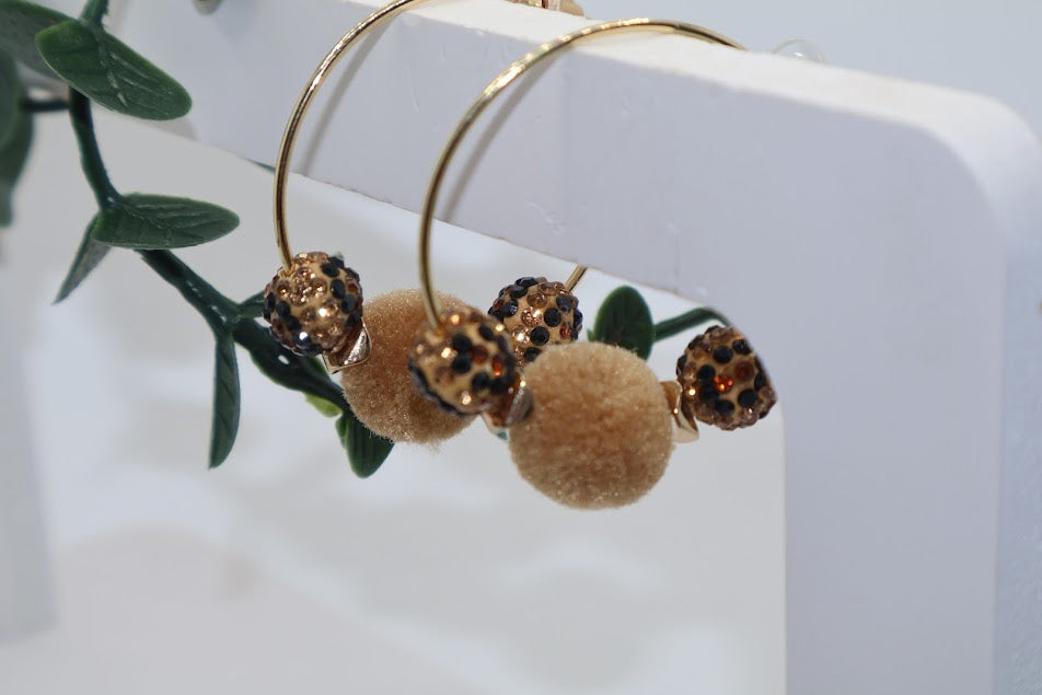Gold hoop earrings with brown spherical charms on a white surface with green leaves.