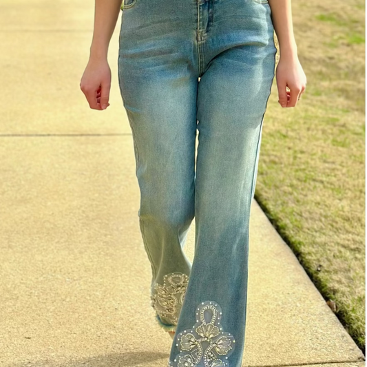Woman wearing a white striped shirt and blue jeans with floral embroidery on a sidewalk.